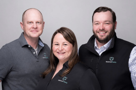 Three people pose together wearing shirts and a vest bearing the Balance Theory logo.